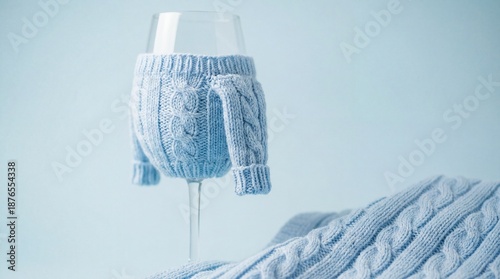 Transparent wine glass wearing a small light blue cable-knit sweater on a matching blue background