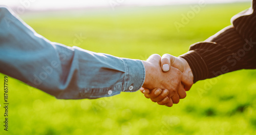 Photos A close-up of two farmers shaking hands against a backdrop of a green agricultural field