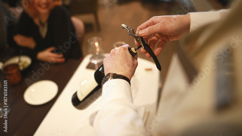 Fotografie Professional waiter opening a bottle of wine with a corkscrew at a luxury fine dining table