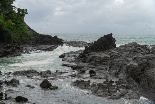 Landscape of the coastal area of Wediombo Beach with trees and massive coral rocks, in cloudy weather. A travel destination in Yogyakarta, Java, Indonesia, Asia.