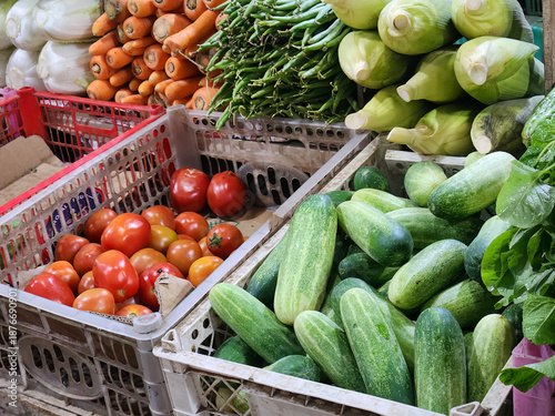 Fresh cucumbers and tomatoes in crates at vegetable market stall. Mixed produce display for grocery shopping and cooking content. Organic vegetables assortment for healthy diet promotion photo.