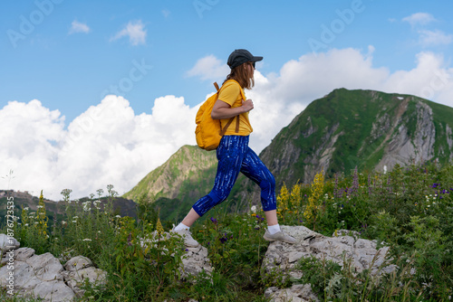 Young woman hiker in a cap with a yellow backpack walking on rocky terrain on a mountain hike in summer, adventure and exploration, Active lifestyle