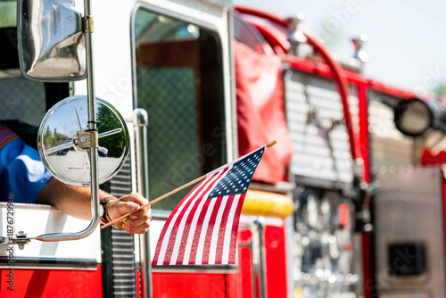 Photography A firefighter waves an American flag from the driver's seat window of a firetruck during a patriotic US parade for Memorial Day, Flag Day, or July 4th