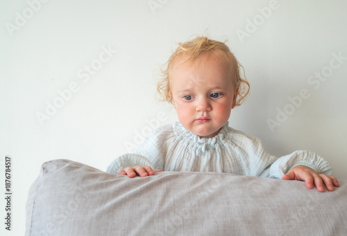 A baby is standing on a pillow and looking at the camera