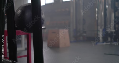 Camera is panning and pulling focus, revealing vertical post with black medicine ball, showing gym