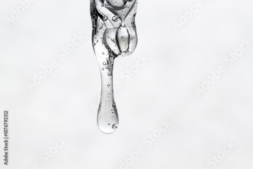 Serum dripping from a pipette, front view, close-up. A drop of cosmetic texture with bubbles.