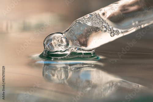 Glass pipette with transparent serum, hyaluronic acid close-up on beige background, front view.