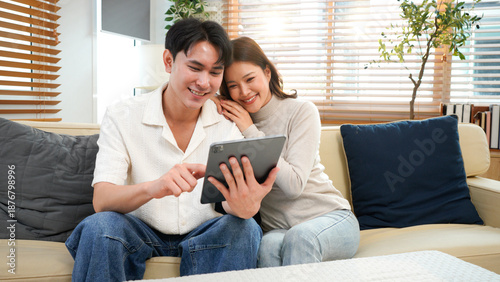 Bild auf Leinwand couple sitting on sofa in home playing tablet and relaxing together