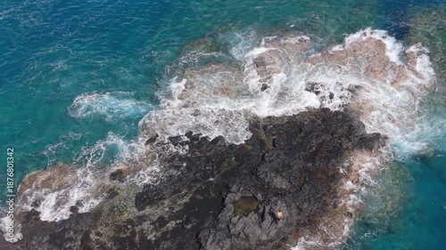 Aerial drone footage showing a lone fisherman standing on volcanic rocks along the coastline in Reunion Island, surrounded by waves and turquoise water. Ideal for outdoor lifestyle visuals