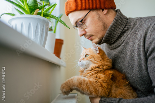 Foto Man holding a fluffy ginger cat by a radiator, both enjoying the comfortable war