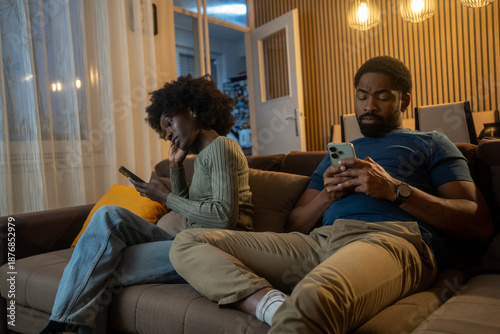 Tableau sur toile Young Black couple using smartphones separately, ignoring each other at home