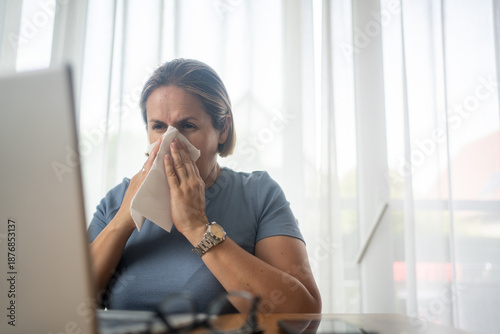 Photos Mature businesswoman using a tissue while sneezing in the office.