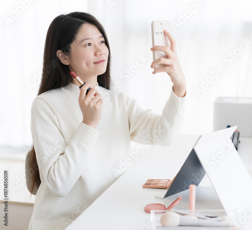 A woman is taking a selfie with lipstick and her phone.