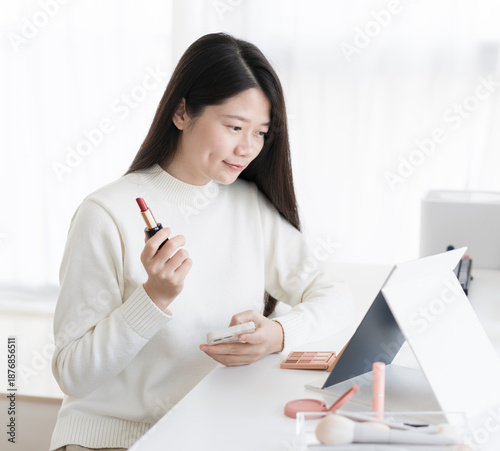The woman is looking at herself in the mirror while holding her lipstick.