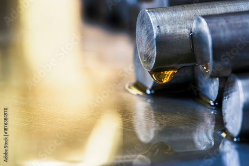 Close-up of stacked precious metal rods covered with machine oil on a metal surface in an industrial environment, showing circular cross sections and metallurgy production concept.