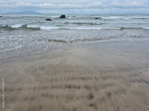 The ocean whispers to the beach as soft surf laps at the damp sand beneath a muted, cloudy sky.