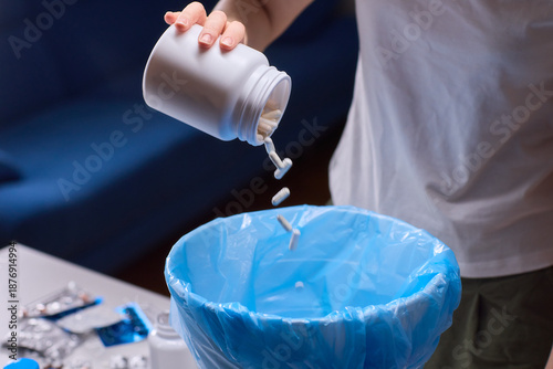 Responsible medication disposal in residential living space, An individual safely discards expired tablets from open containers into trash in living room setting