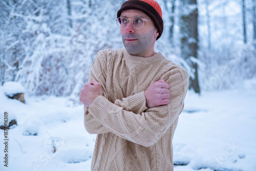Obraz na plátně Young man in beanie and sweater shivers in snowy forest, looking lost and cold,