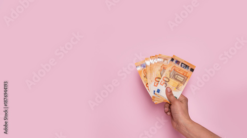 фотографія Horizontal web banner of a hand holding euro banknotes on a pastel pink background with copy space