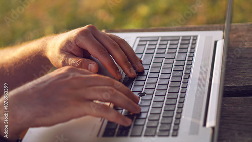 Close-up of digital nomad freelancer hands typing on laptop. Close-up of hands typing on a laptop outdoors on a wooden table.