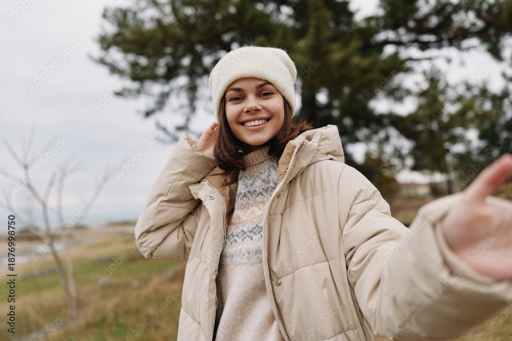 Fototapeta premium Woman outdoors in a warm coat and beanie, smiling in a windy countryside landscape. Casual fashion, cozy vibe, and relaxed portrait captured with natural light in an open field.