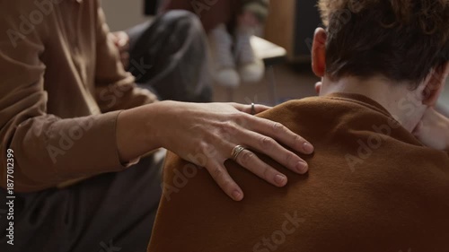 Close up on hand of female psychotherapist resting gently on teenage boys shoulder offering reassurance during emotional moment in therapeutic group session for adolescents