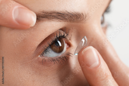 Fotografie Woman putting on contact lenses against light background, closeup