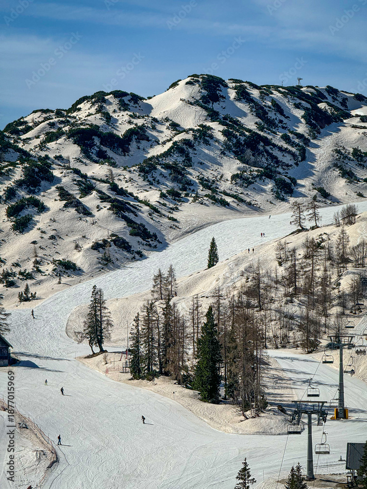 Fototapeta premium Alpine ski resort where white snow is tinted brown after African dust storm. Chairlifts, pistes, and rugged mountains illustrate unusual weather patterns and environmental change during late winter.