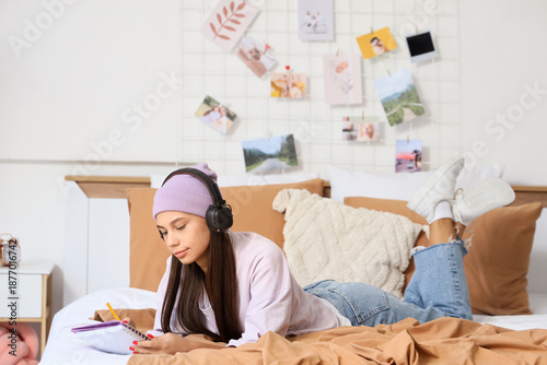 Teenage girl with headphones writing on notebook in bedroom
