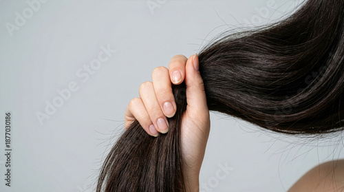Woman holds long dark hair with one hand while standing against a plain background during daytime