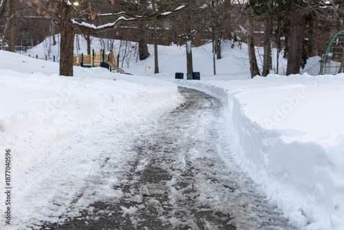 Winter road in the park with salt and melting snow. Pathway in residential neighborhood.