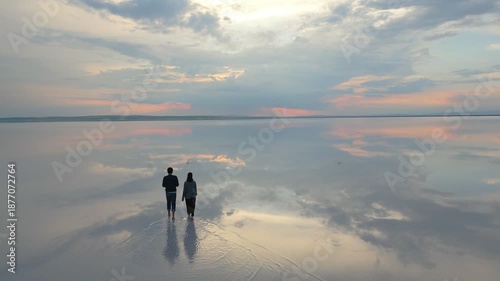 Couple walking barefoot on Tuz salt lake enjoying a stunning sunset reflection drone aerial view in Turkey