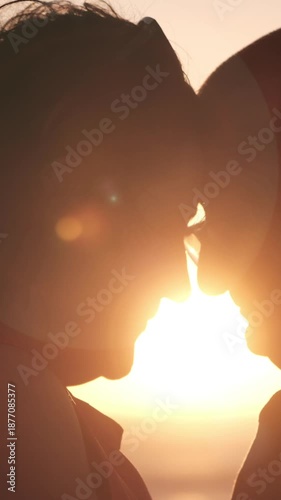 Vertical Romantic cinematic video with gentle animated zoom on a silhouetted couple at sunset, enhanced by warm lens flare and soft golden light for an emotional, atmospheric stock feel.