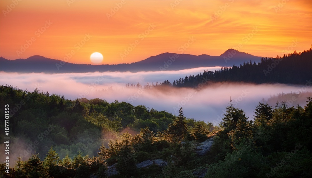 Obraz premium mist covered evergreen mountains under a glowing orange sky capturing a serene and mystical atmosphere at dawn or dusk
