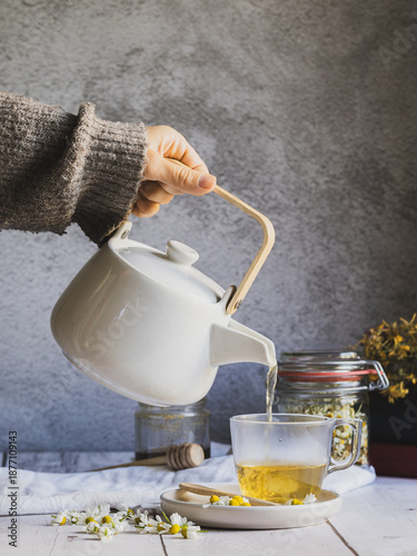 A woman's hand pouring a cup of chamomile tea, preparing a moment of relaxation and self-care.