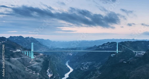 Aerial time-lapse of a majestic suspension bridge spanning a deep canyon with dramatic mountain scenery and soft dusk lighting, Huajiang Canyon Bridge in Guizhou Province, China