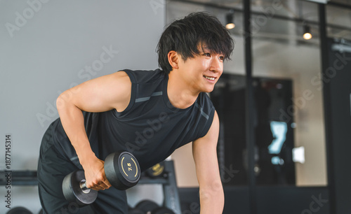 Bild auf Leinwand Young Asian man doing dumbbell training at fitness gym