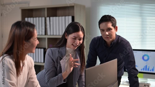 Three people are standing around a laptop computer. One of the people is pointing at the screen. The other two people are looking at the screen