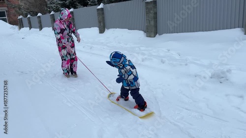 A mother teaches a little boy to snowboard.