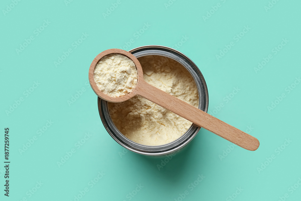 Fototapeta premium Container of powdered milk with wooden measuring scoop on turquoise background