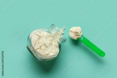 Jar of powdered milk with measuring scoop on turquoise background © Pixel-Shot