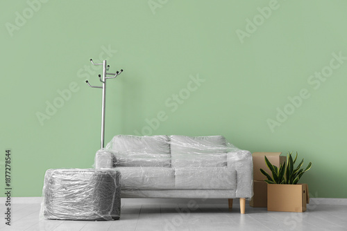 Grey sofa and pouf wrapped in stretch film with rack near green wall