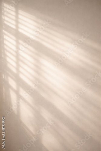 Warm sunlight casting abstract shadows of window blinds on a light beige wall, creating a serene and minimalist aesthetic.