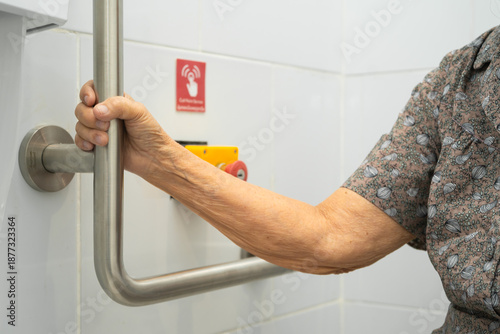 Asian elderly woman use toilet security support rail in bathroom.