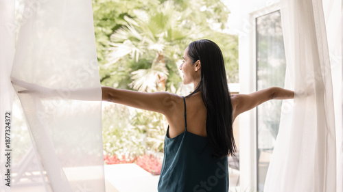 Tableau sur toile Happy young Maori woman opening veils at window or glass door, looking at terrace view, tropical greenery, enjoying vacation, holiday, weekend in hotel on modern resort