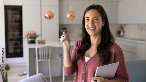 Tableau sur toile Portrait of cheerful woman stands in modern kitchen, smiling while holding keys