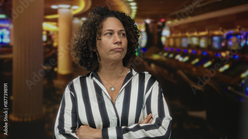 Fotografie Woman wearing striped shirt crossing arms in front of illuminated slot machine row at casino; rejection