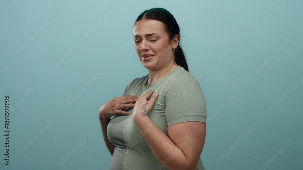 Obraz premium Woman displaying a gesture of disgust against a blue background, wearing a light green shirt, exemplifying negative emotion and body language in a simple studio setup.