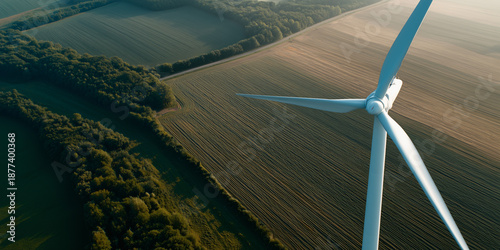 An eye-level view of wind turbine generating renewable energy. Blades spin against the backdrop of fields and trees