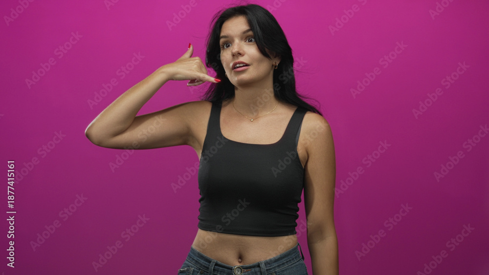 Obraz premium Woman showing call gesture with thumb and index finger like a phone while posing in a pink studio; communication.